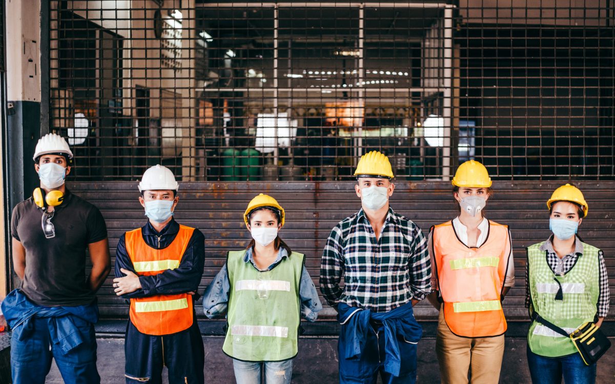 Grupo De Trabajadores Industriales O De Ingenieros Corporativos Con Máscara De Protección Y Casco De Pie En Línea Frente A Una Fábrica De Cierre De Prevención De Un Brote De epidemic De Coronavirus O Covid 19