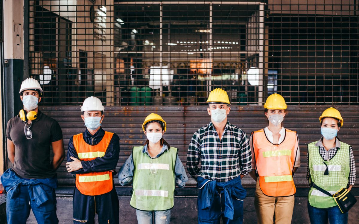 群工业或工程师企业工人穿戴防护面具和安全帽头盔排队站在工厂面前锁定预防冠状病毒或Covid 19疫情爆发