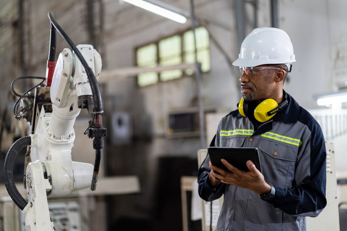 非裔美国男性工程师工人使用数字平板电脑控制自动机械手在工厂的工业机器人安全